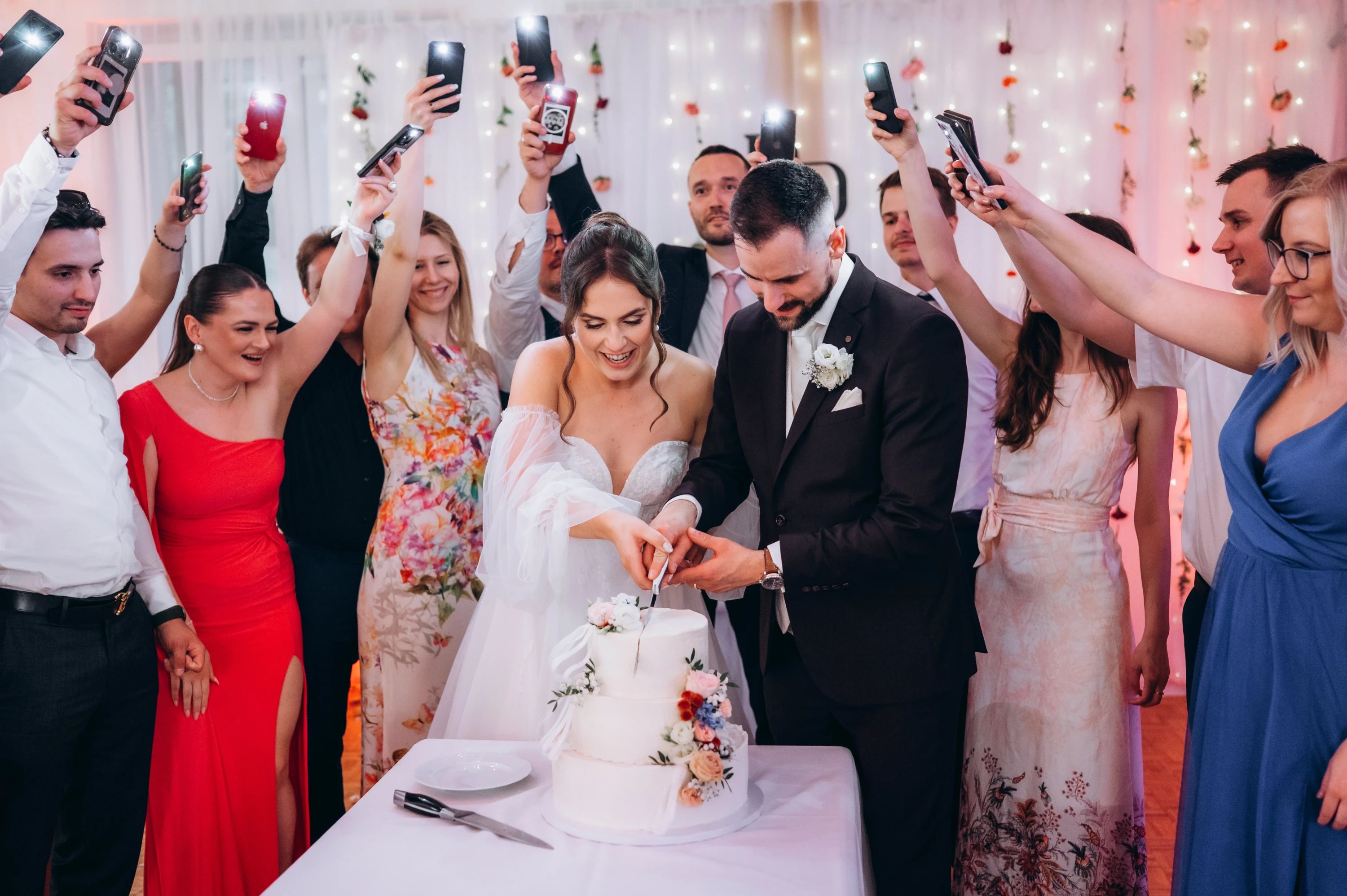 Hostia fotografujú rezanie svadobnej torty novomanželmi.