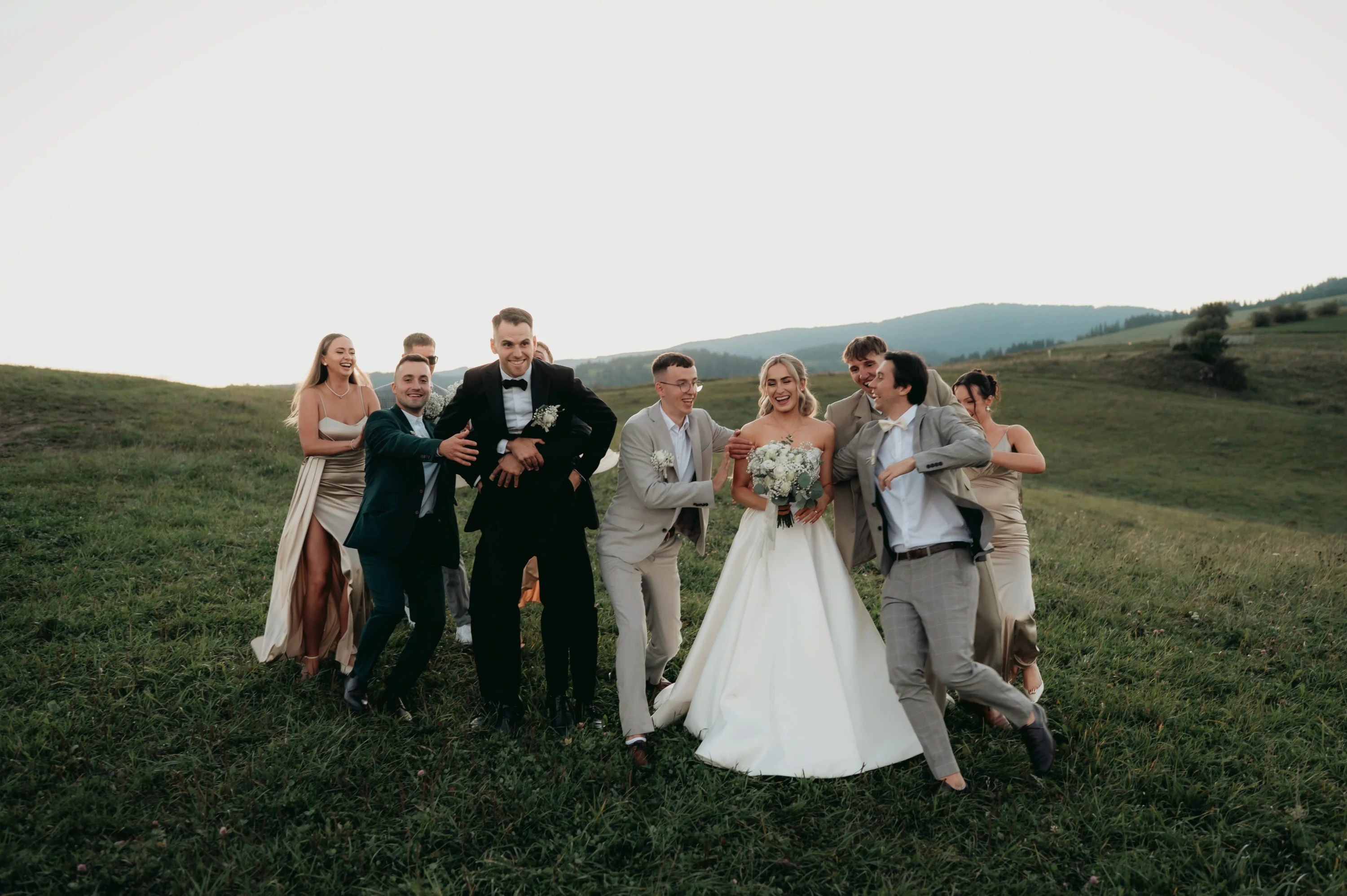 Novomanželia s rodinou a hosťami stoja v poli.