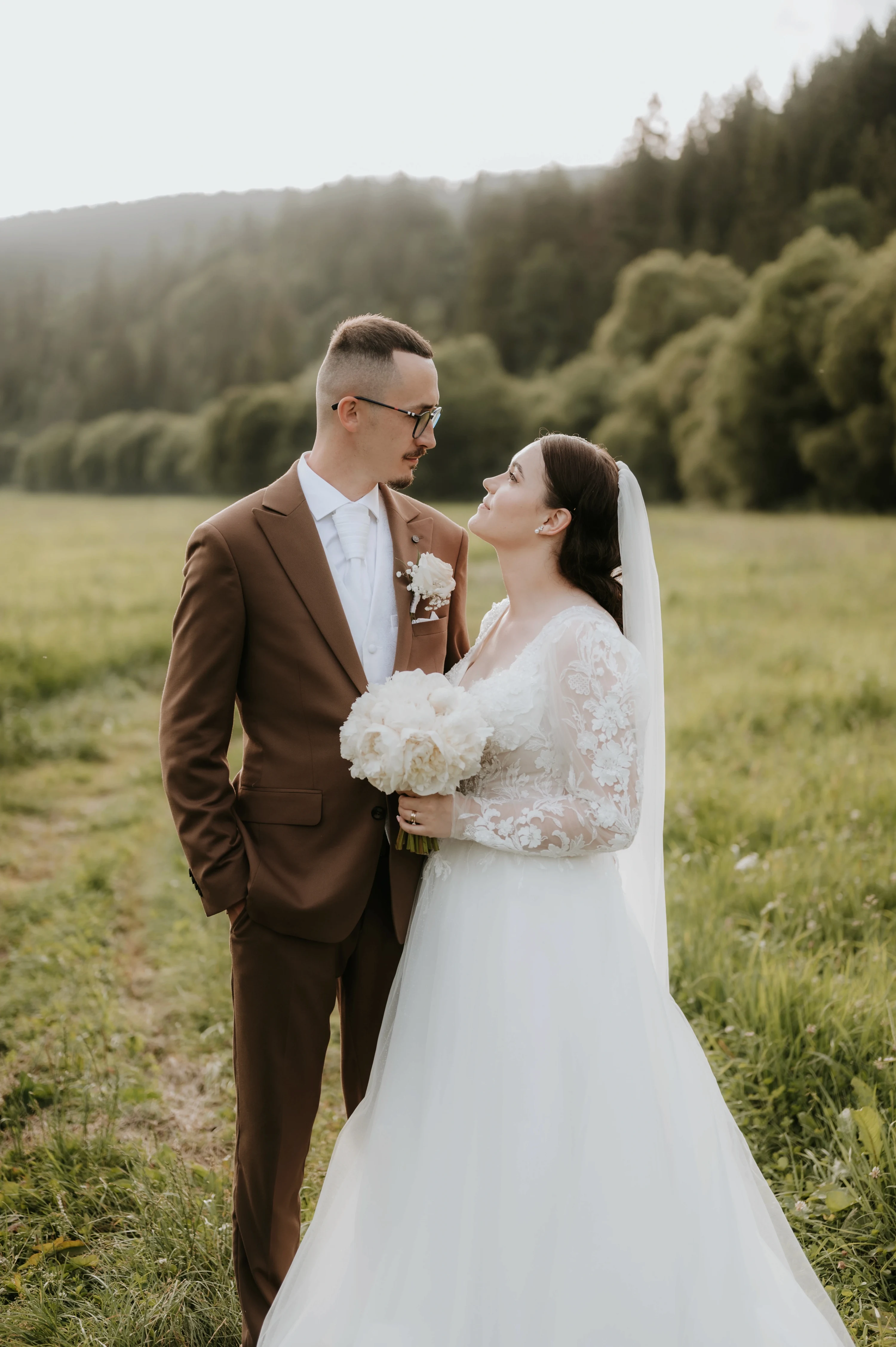 Pár pózuje na lúke pred horami, nevesta sa usmieva.