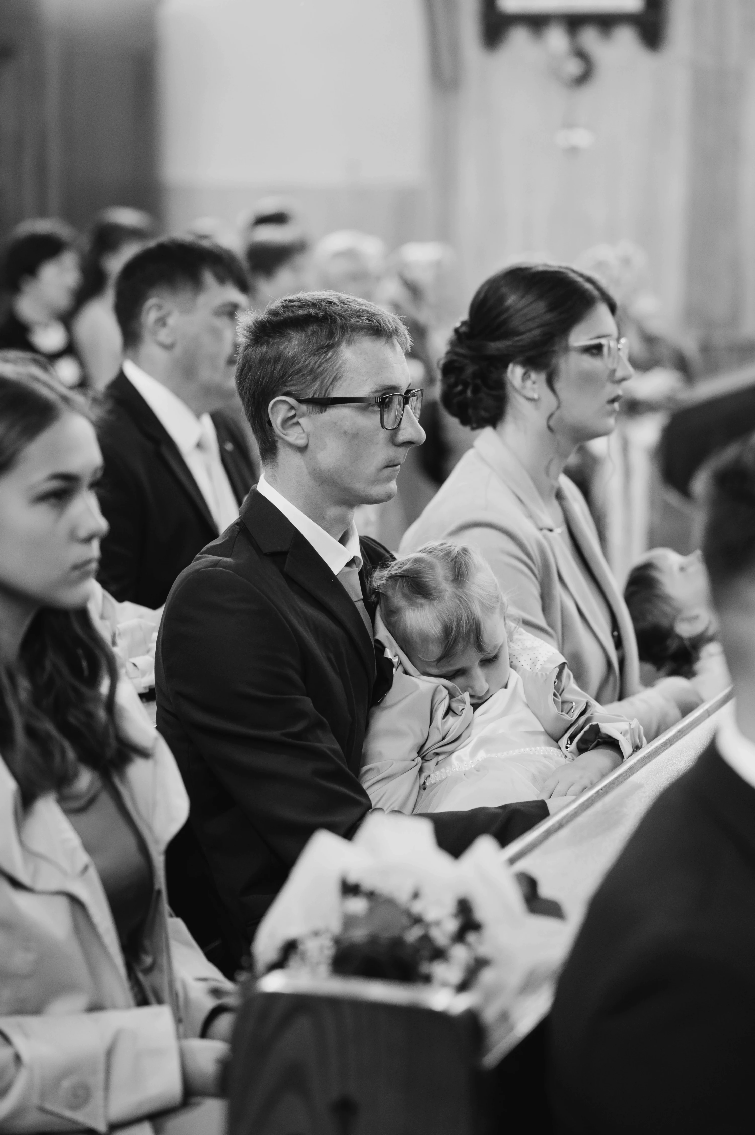 Počas svadobnej ceremónie muž s okuliarmi drží malé dieťa vedľa seba.