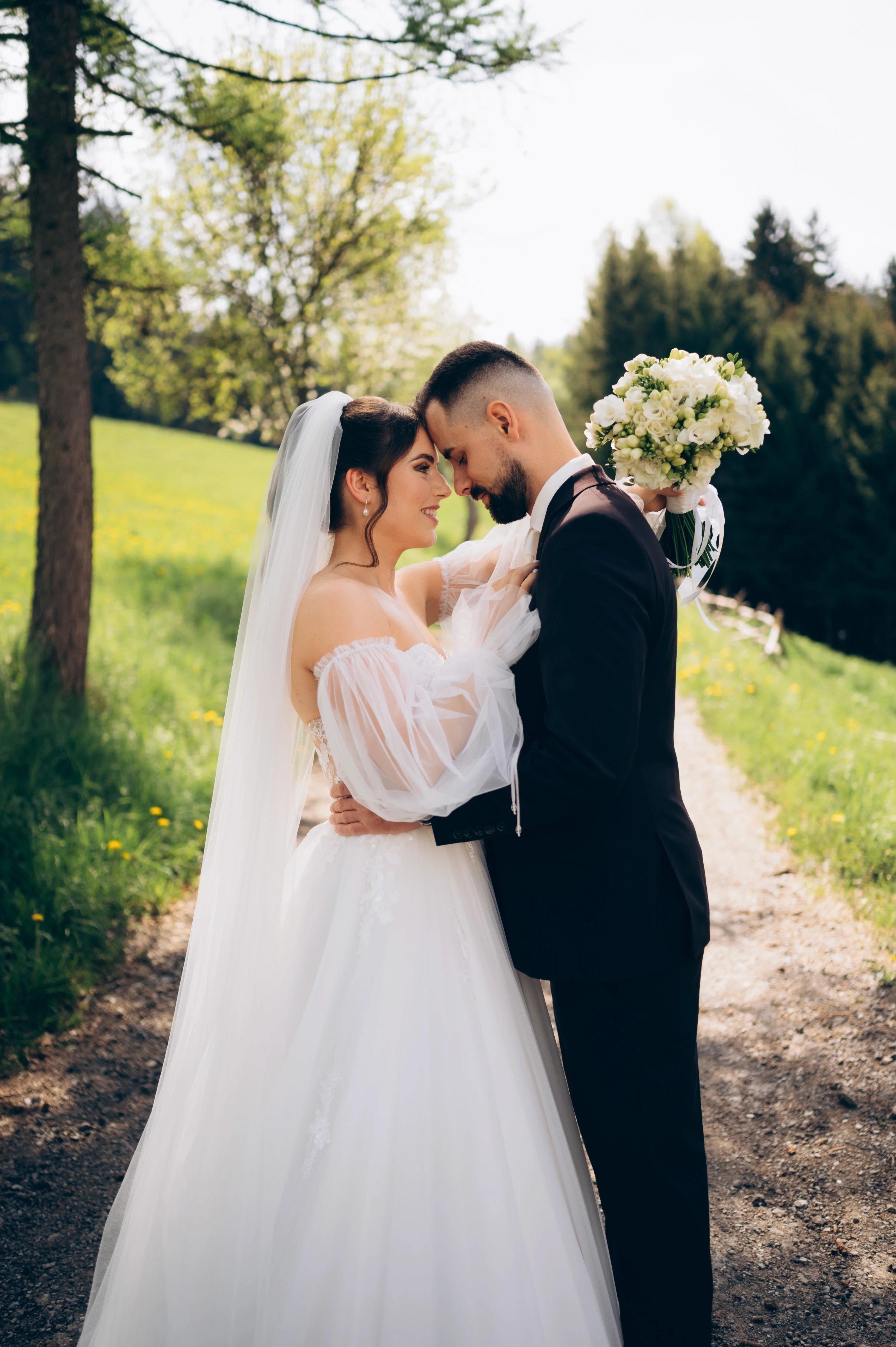 Ženích v čiernom obleku a nevesta v bielych svadobných šatách sa objímajú.