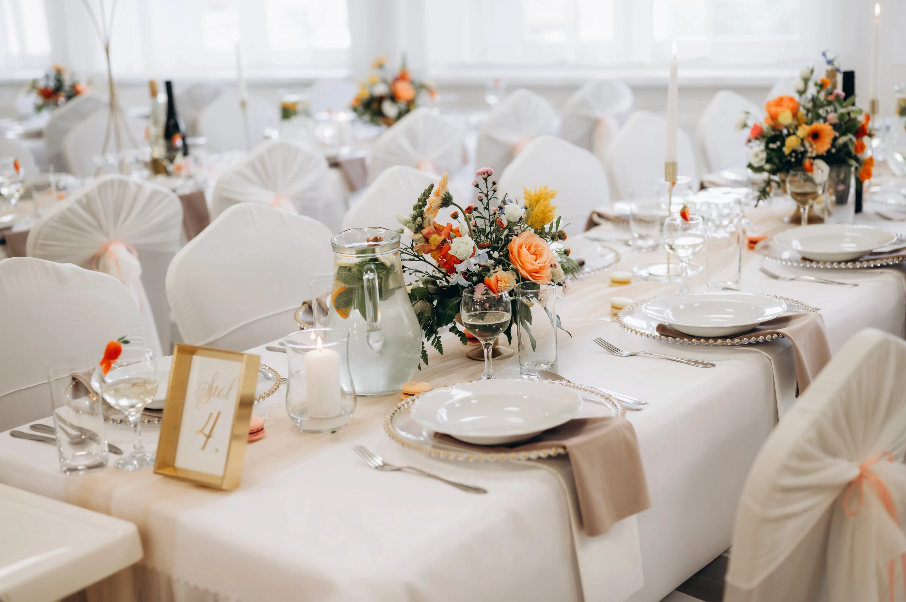 Svadobný stôl s elegantným porcelánom a oranžovými kvetinami.