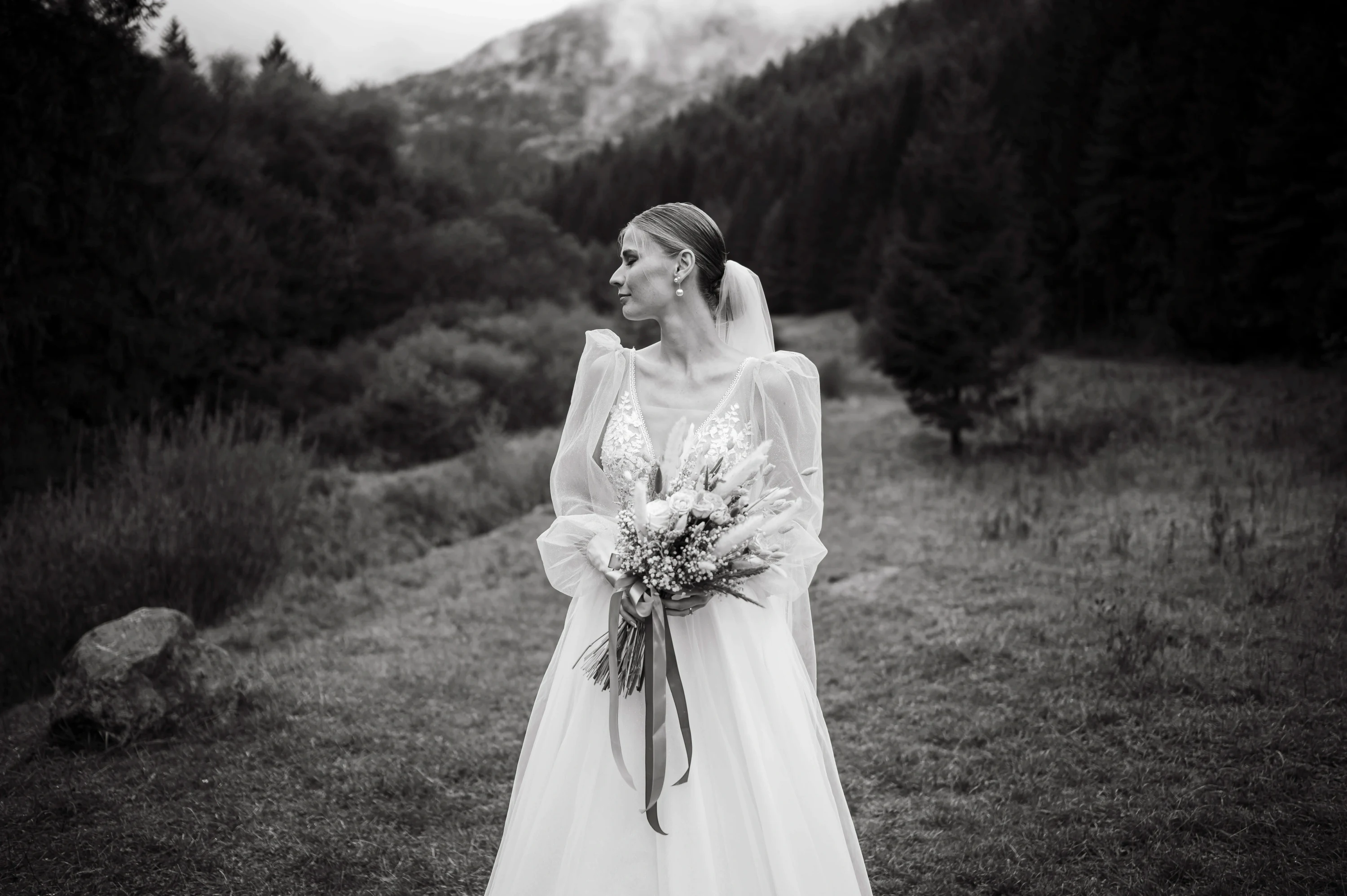 Nevesta v horách drží kyticu na čiernobielej fotografii.
