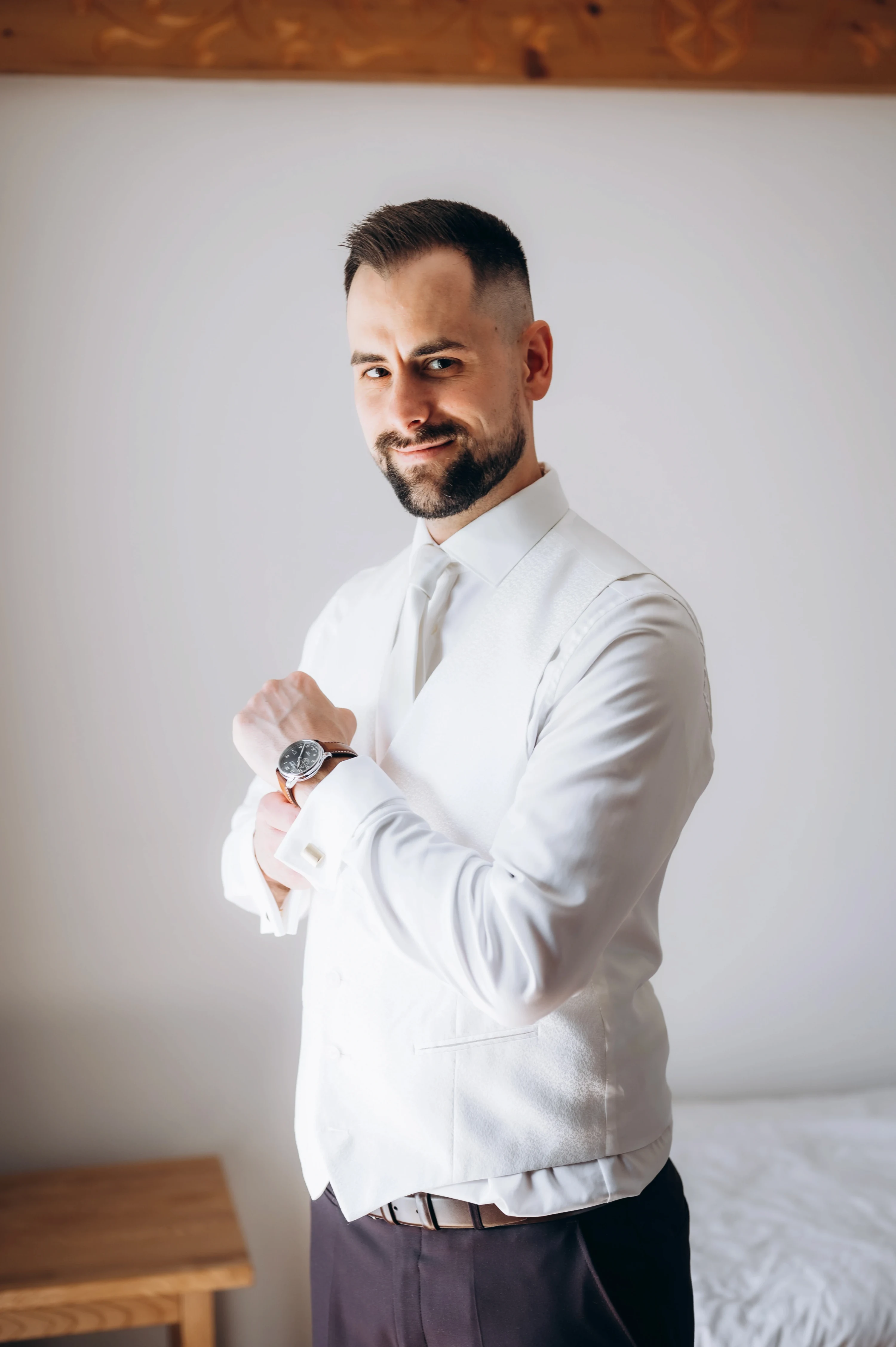 Ženích v bielej košeli si s úsmevom kontroluje hodinky pred svadbou.