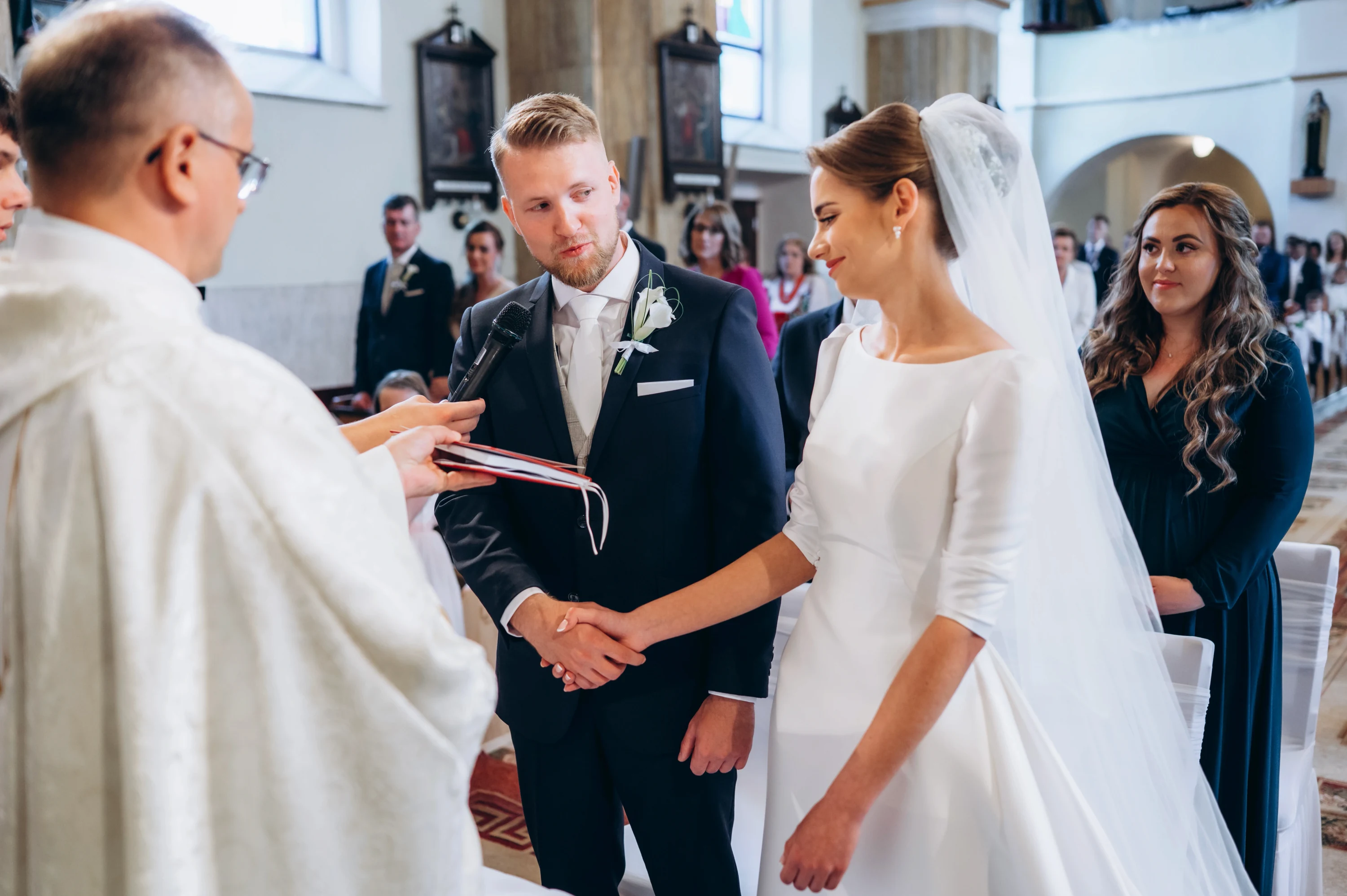 Kňaz s červenou knihou spája ruky ženícha a nevesty počas manželského sľubu.