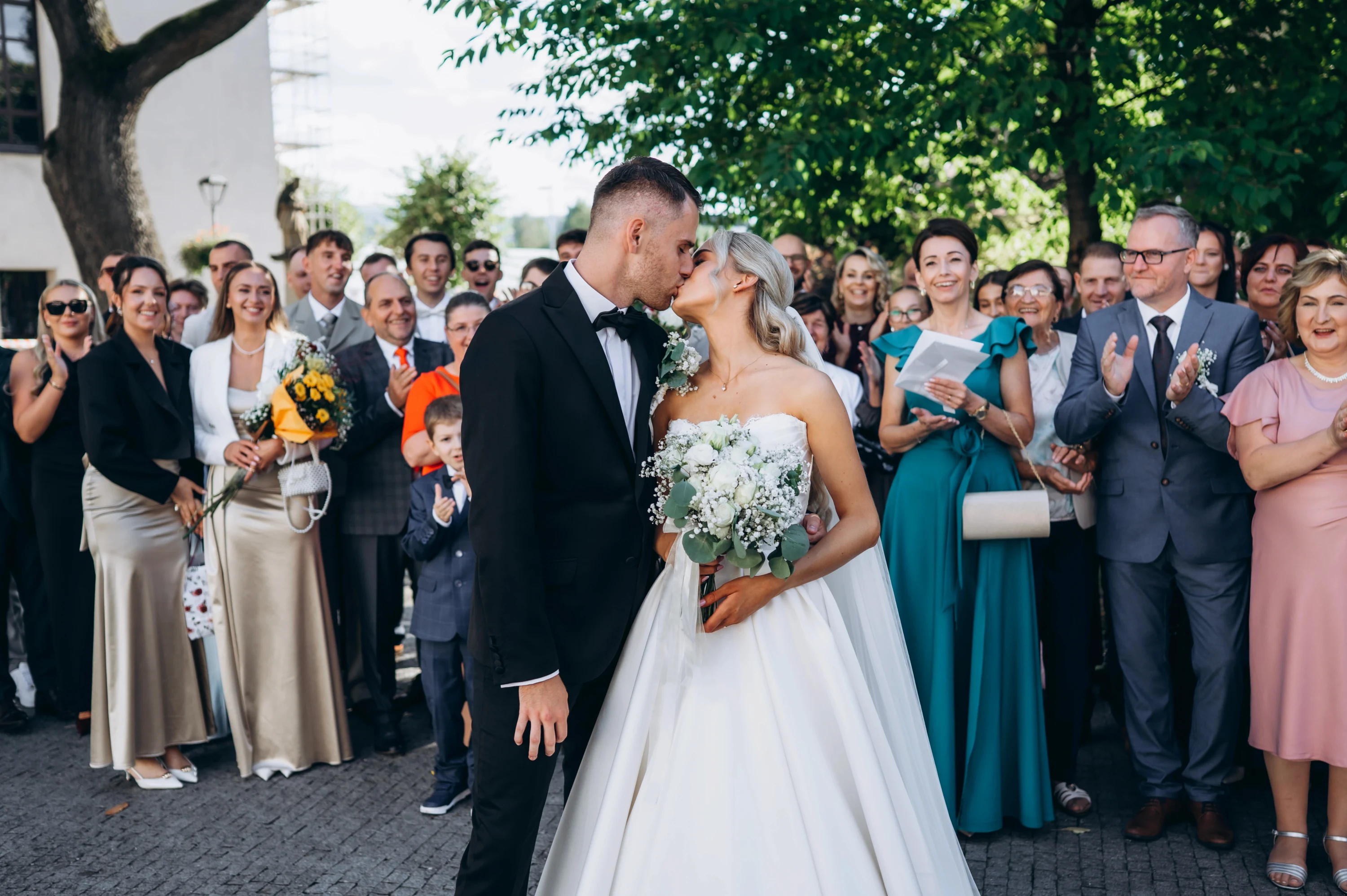 Nevesta a ženích sa objímajú s hosťami okolo.