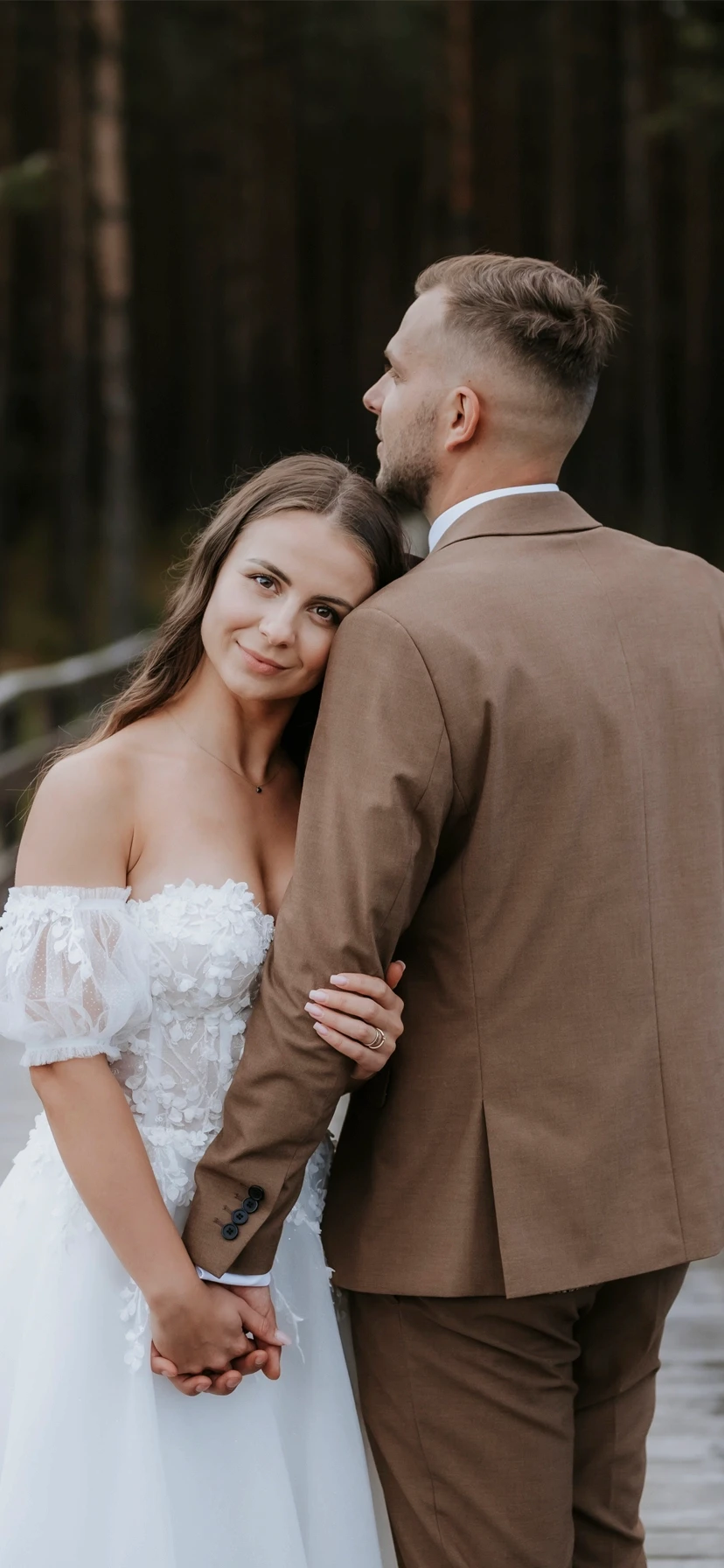 Nevesta sa usmieva a drží sa za ruku s ženíchom v lesnom prostredí.