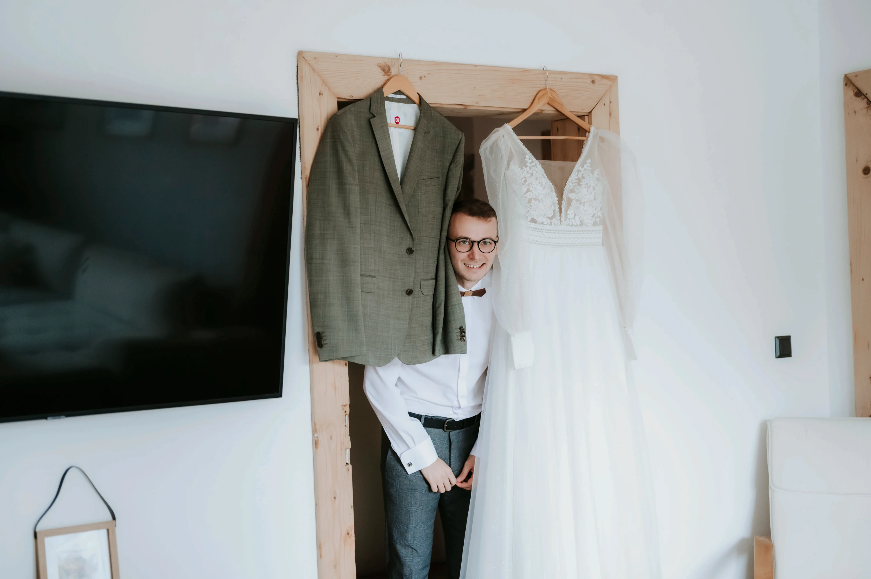Muž ukrytý za visiacimi svadobnými odevmi.