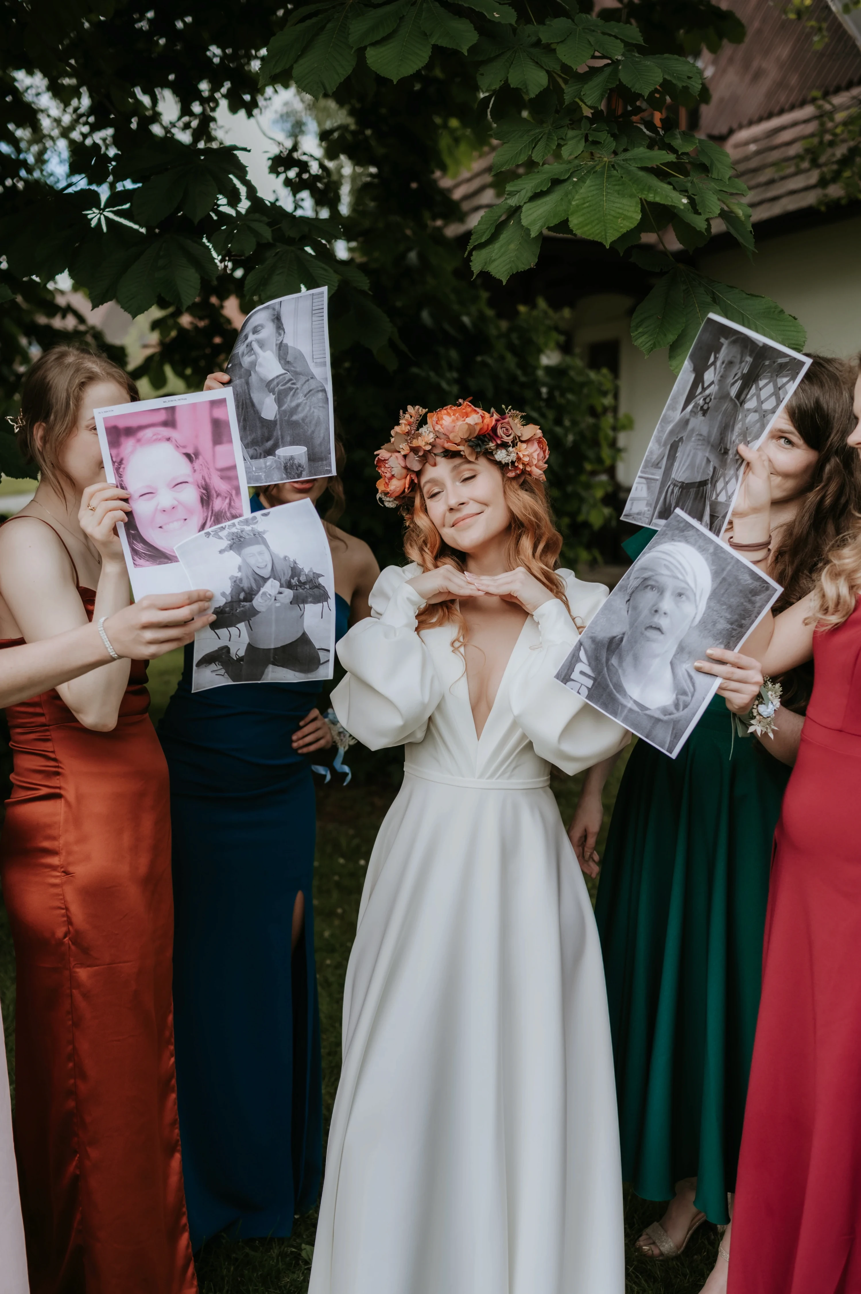 Družičky držia pred tvárami detské fotografie, nevesta s vencom sa medzi nimi usmieva.