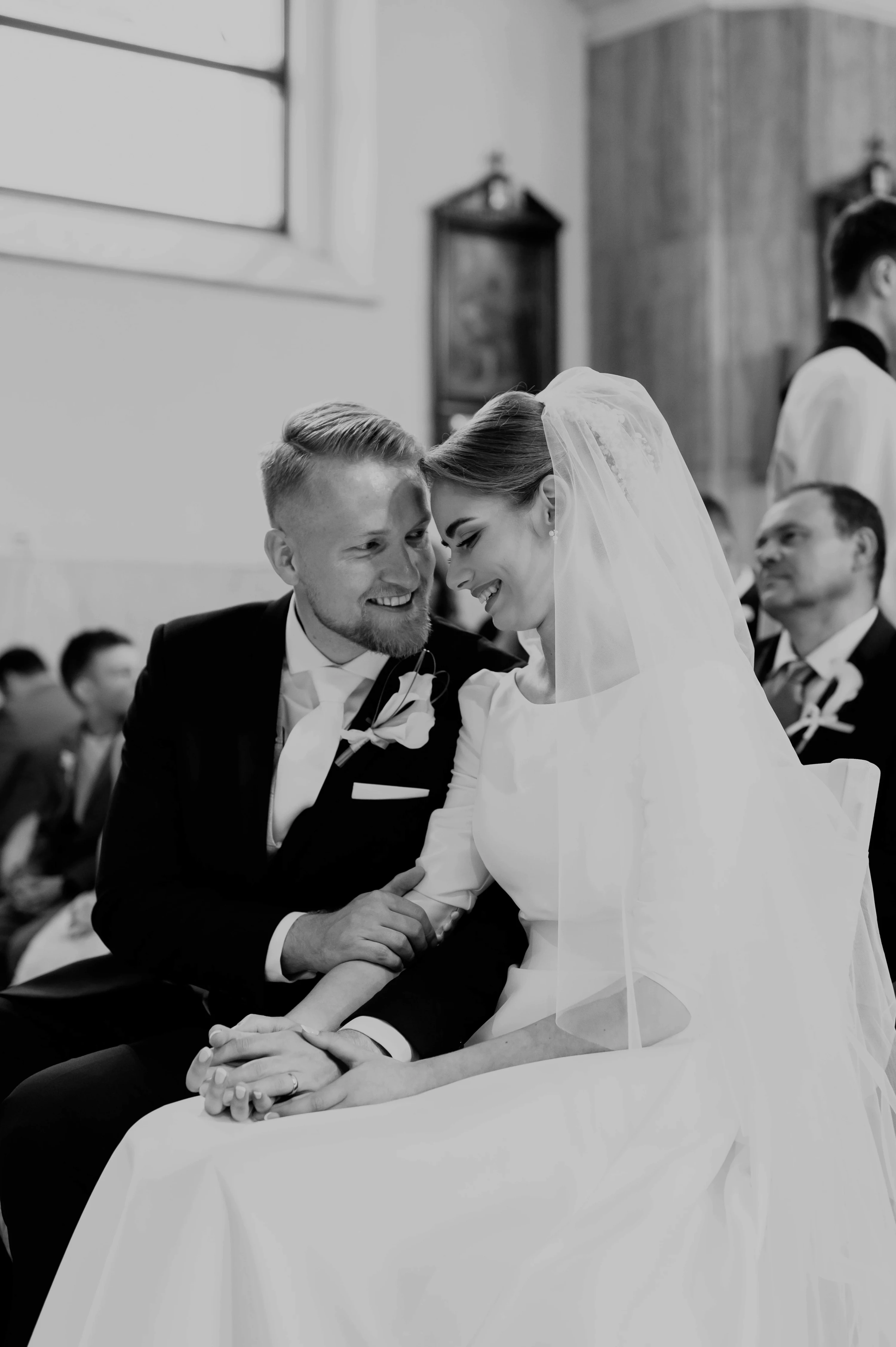 Nevesta a ženích sedia počas obradu a usmievajú sa na seba.