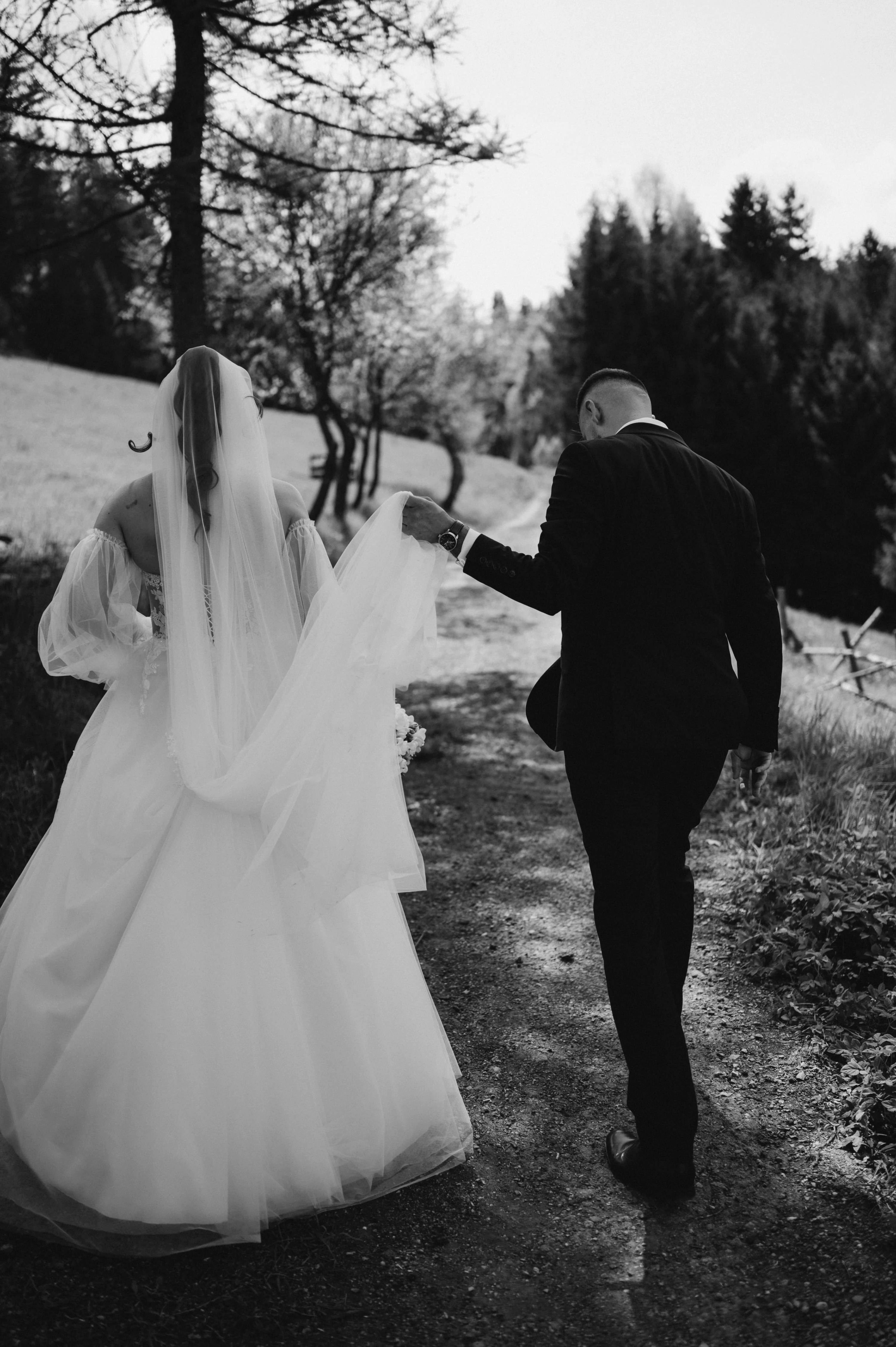 Novomanželia sa prechádzajú lesnou cestou s nevestou v závoji.