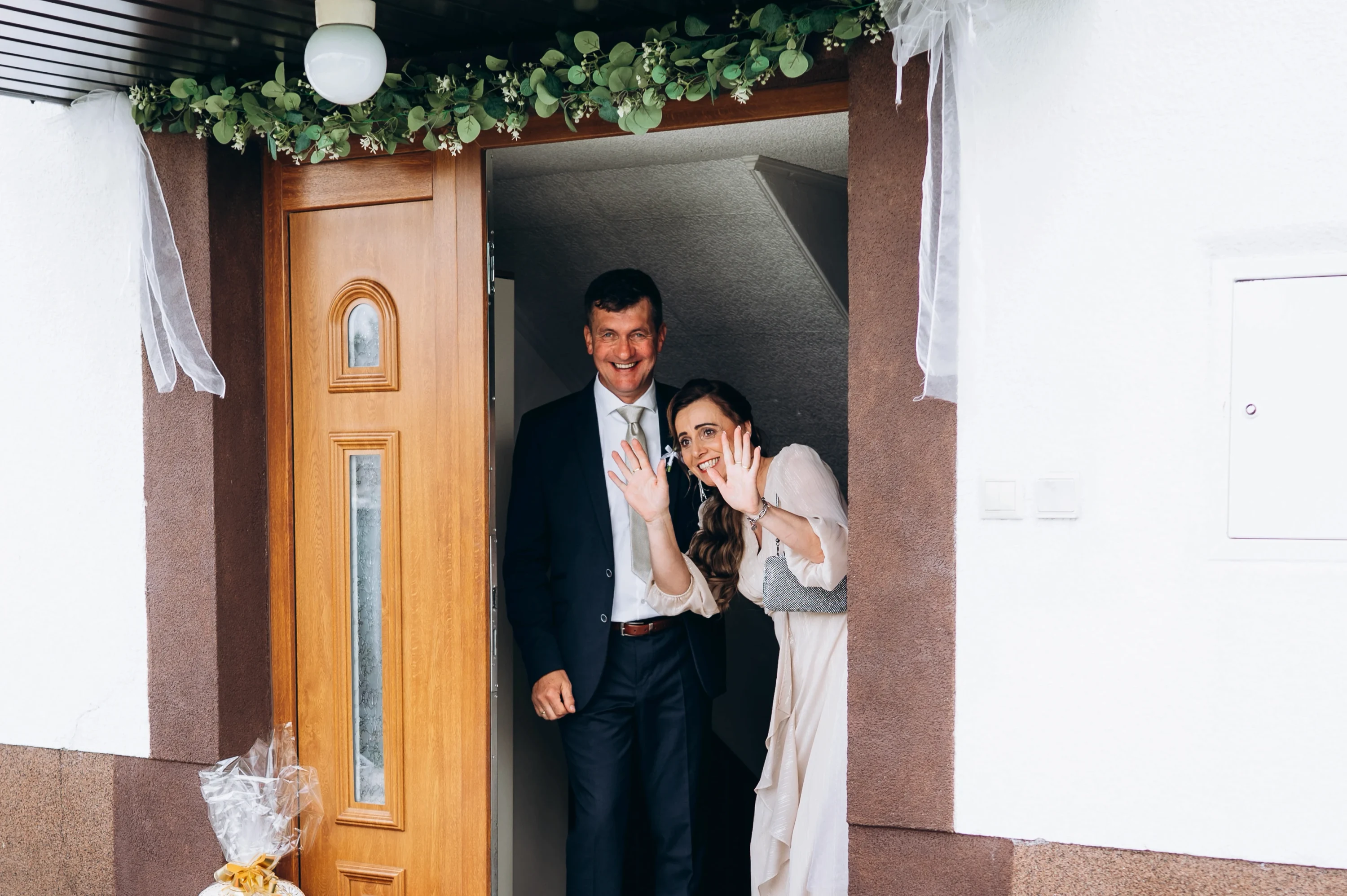 Dvojica máva z domových dverí ozdobených eukalyptovou girlandou a tylom.