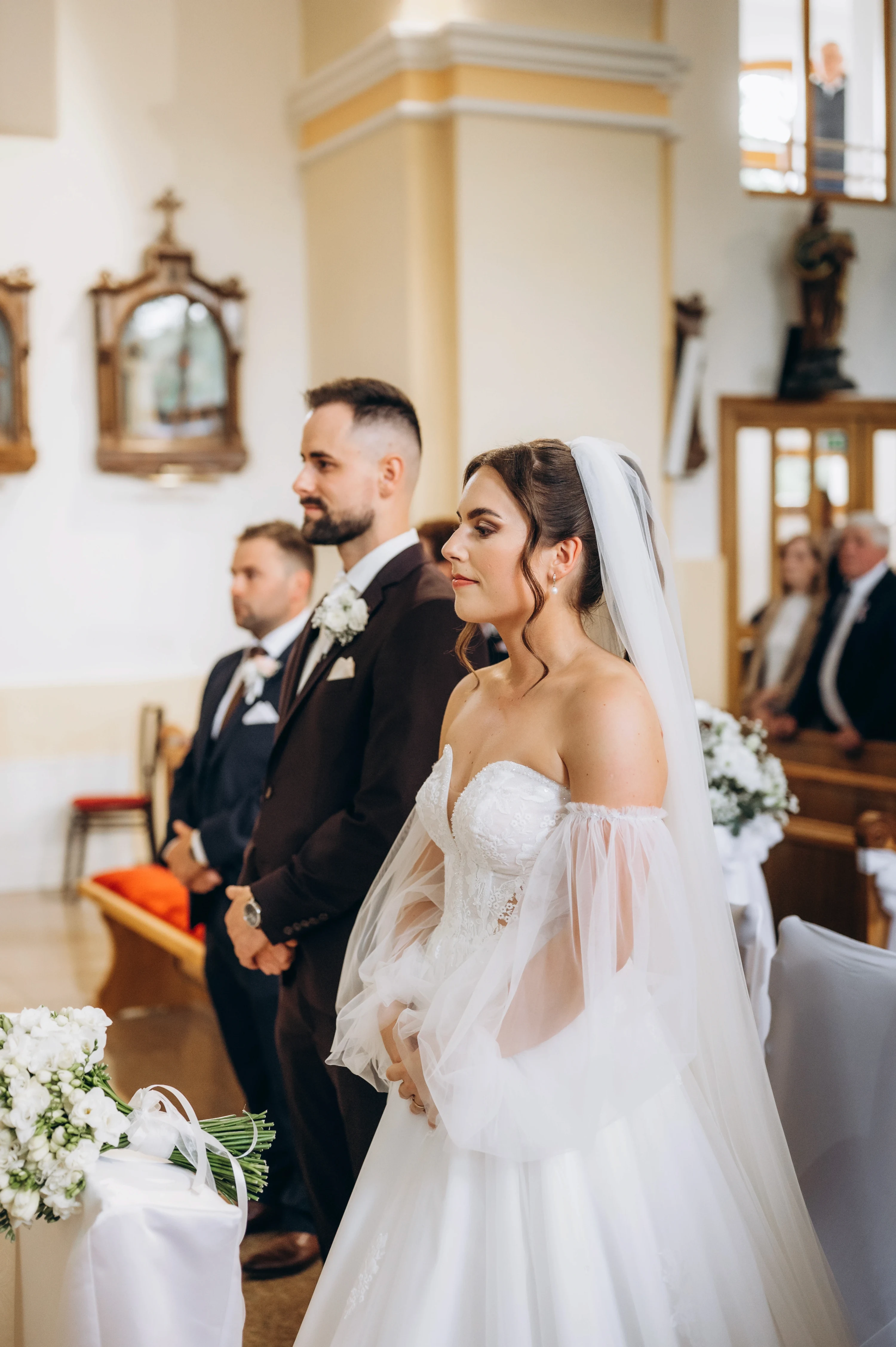 Nevesta so ženíchom stoja počas obradu v kostole, v popredí kytica bielych kvetov.