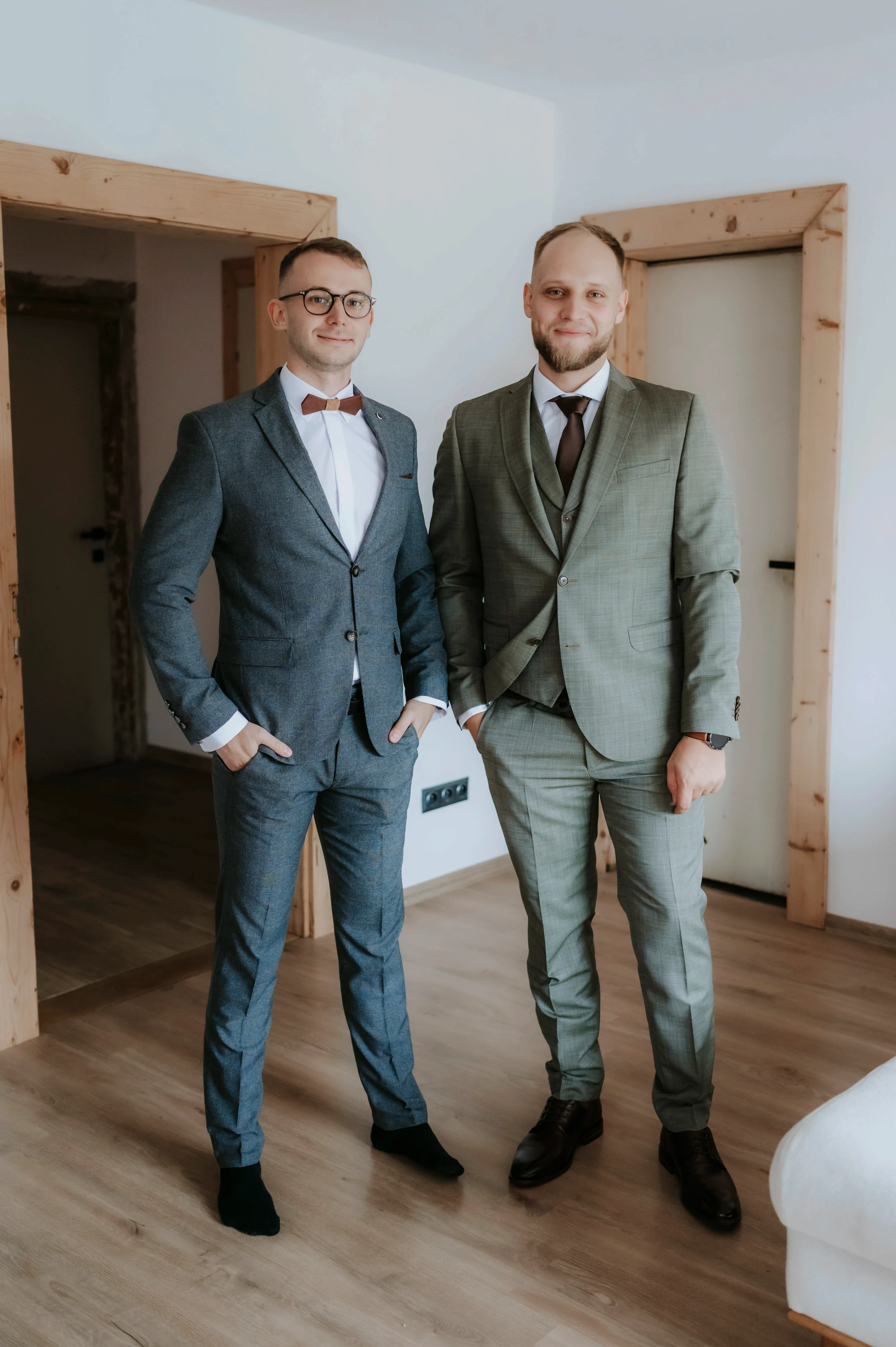 Dvaja muži vo svadobných oblekoch stoja vedľa seba.