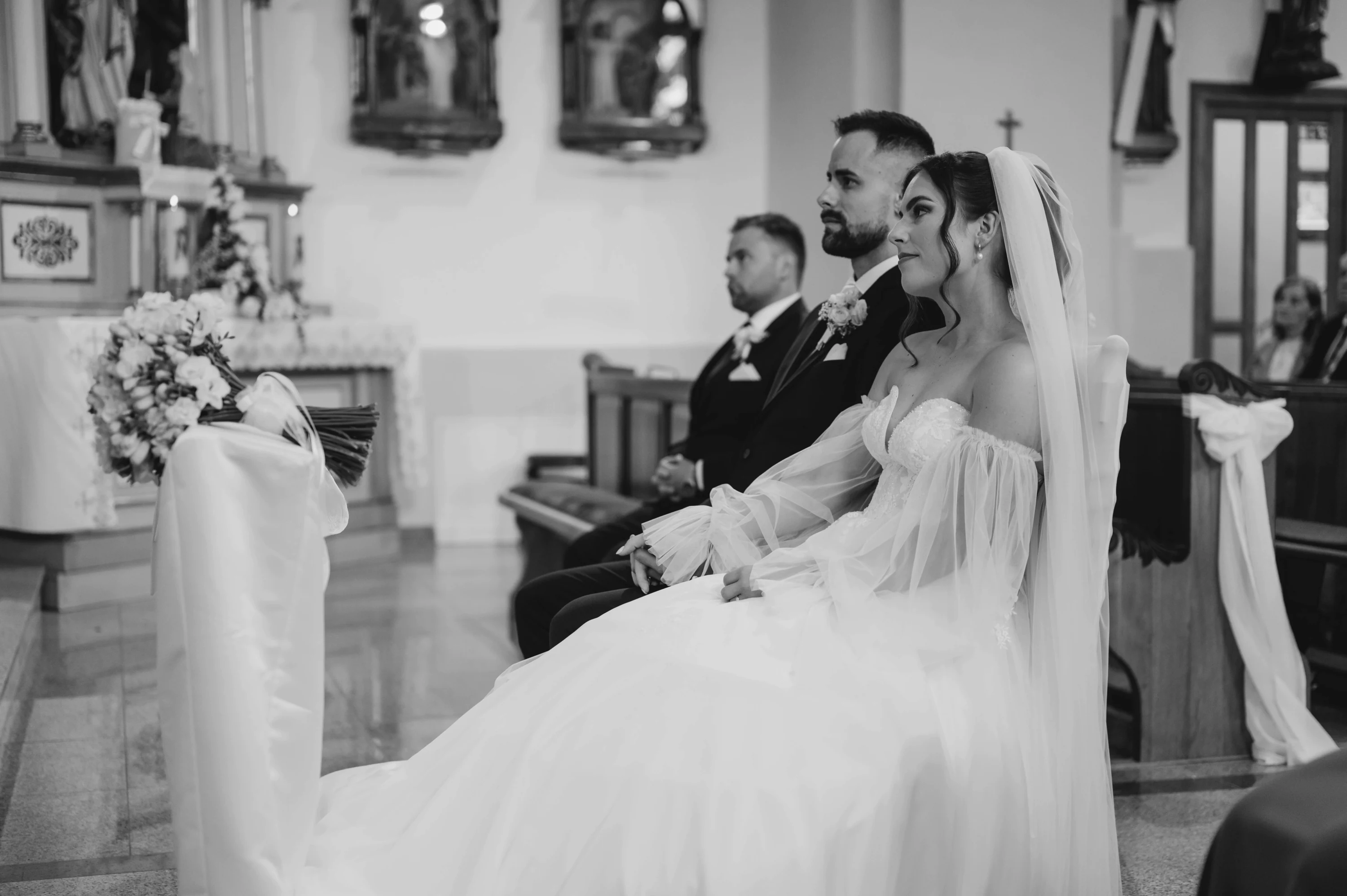 Čiernobiely záber: pár sa drží za ruky pri oltári v chráme počas obradu.