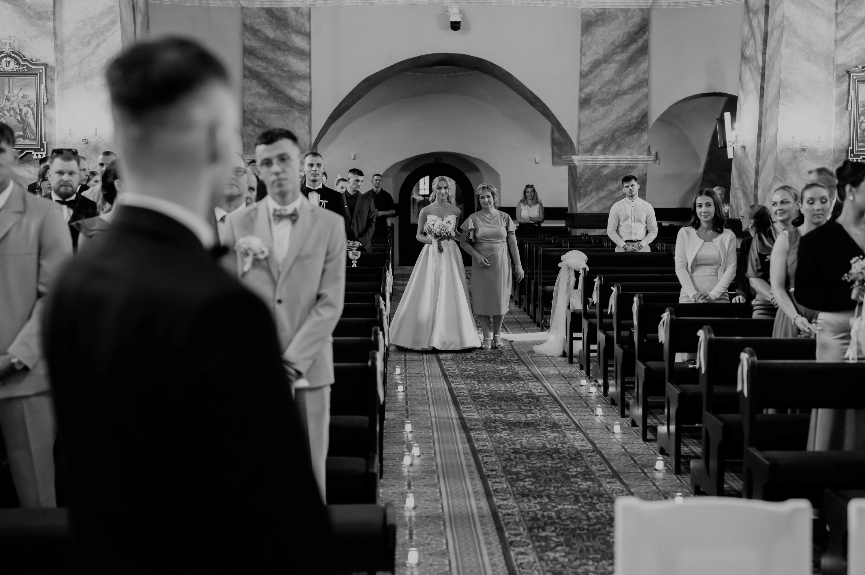Nevesta kráča kostolnou uličkou k ženíchovi, čiernobiely záber.