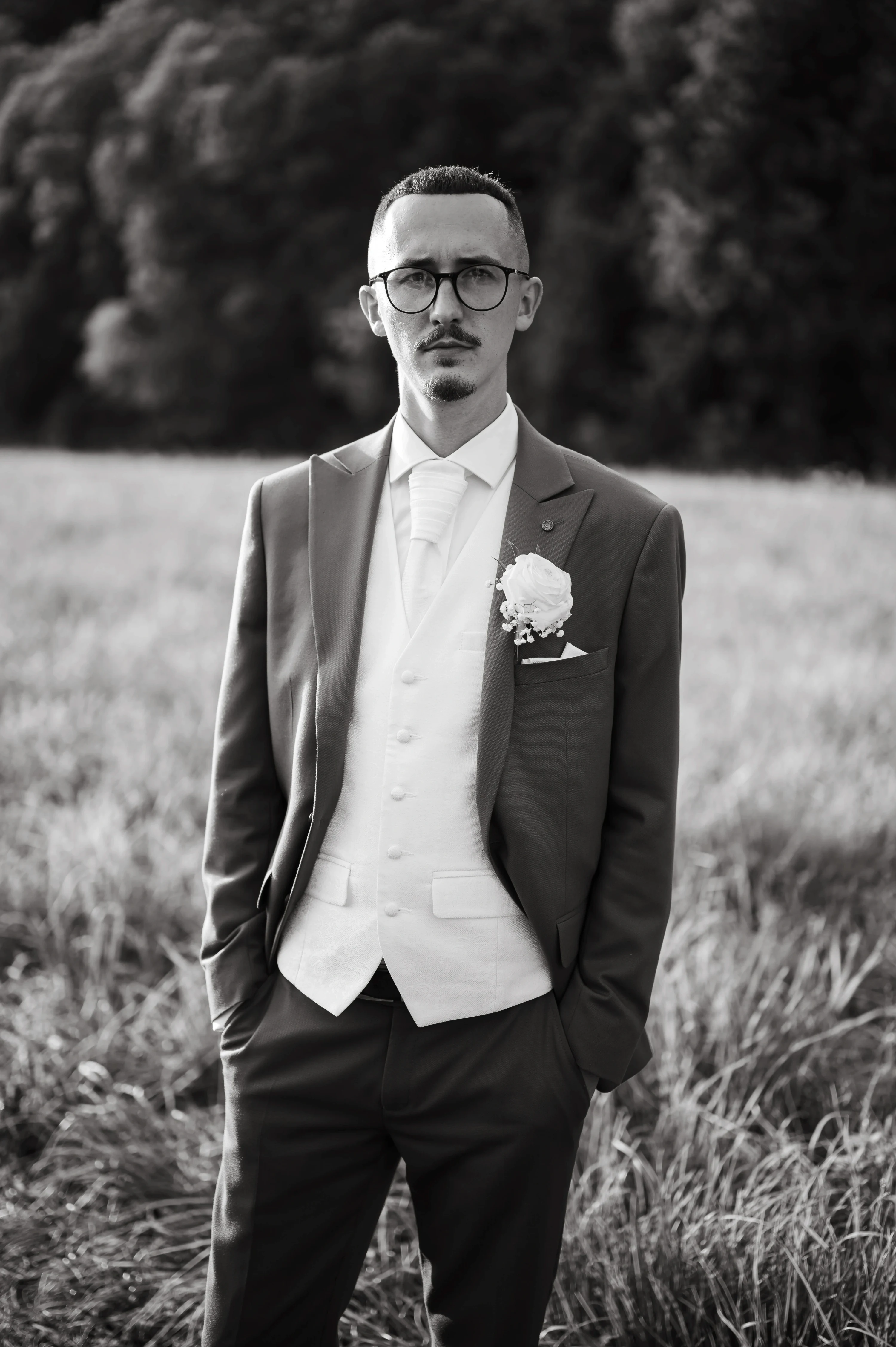 Čiernobiely portrét ženícha v elegantnom obleku na lúke.