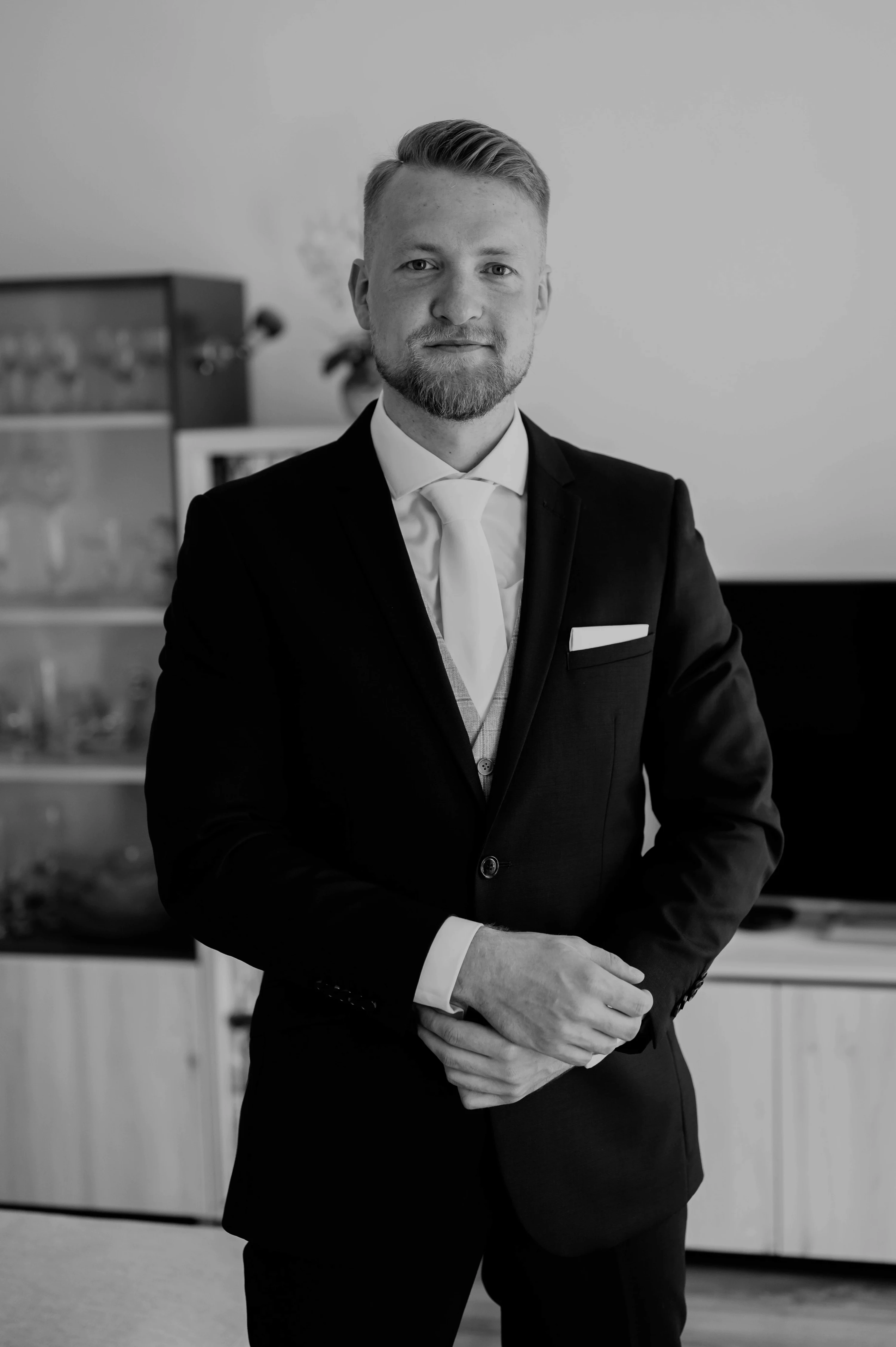 Čiernobiely portrét ženícha v tmavom obleku so svetlou kravatou v obývačke.