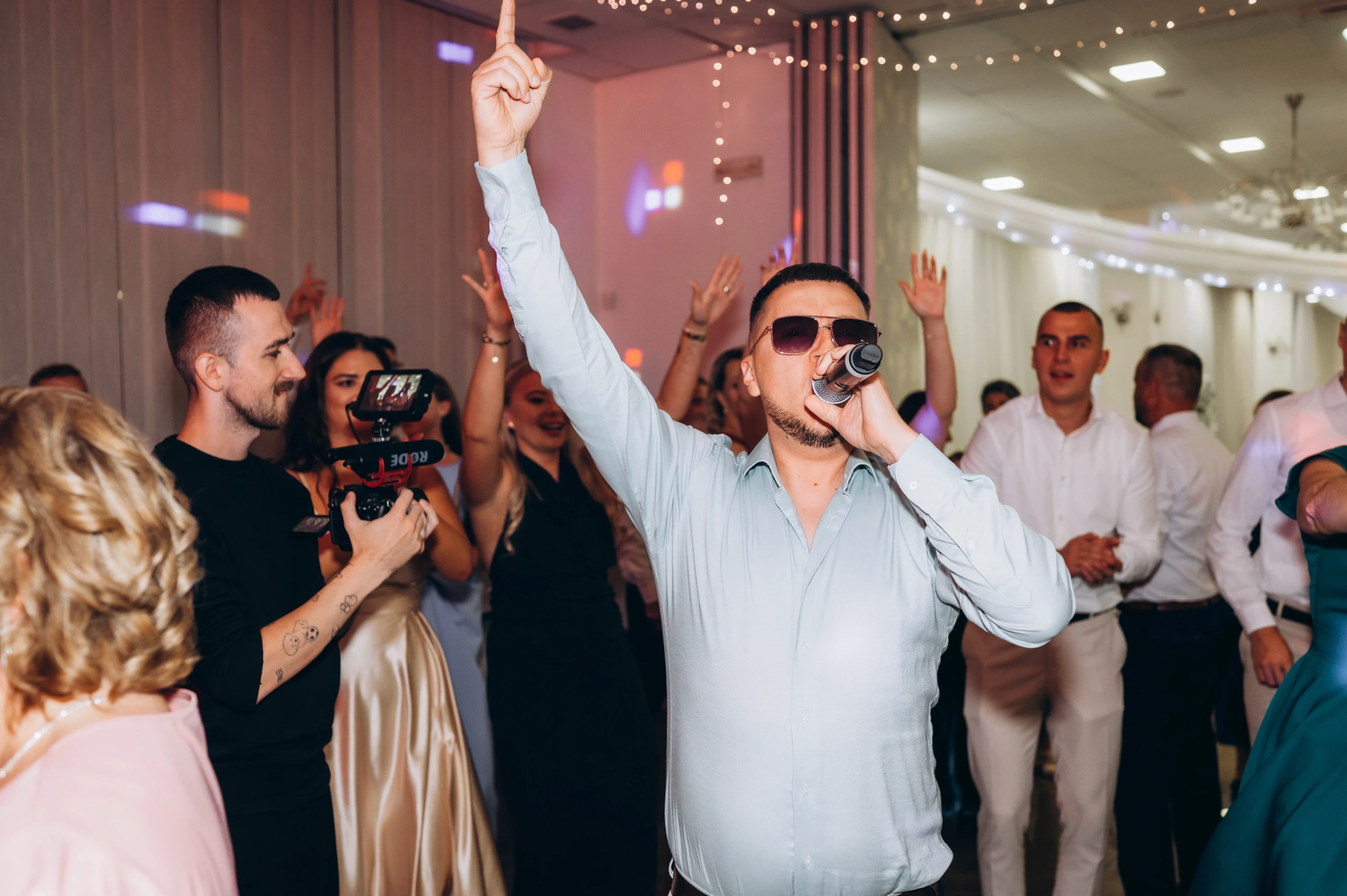 Hosť radostne spieva pri mikrofóne na hostine.