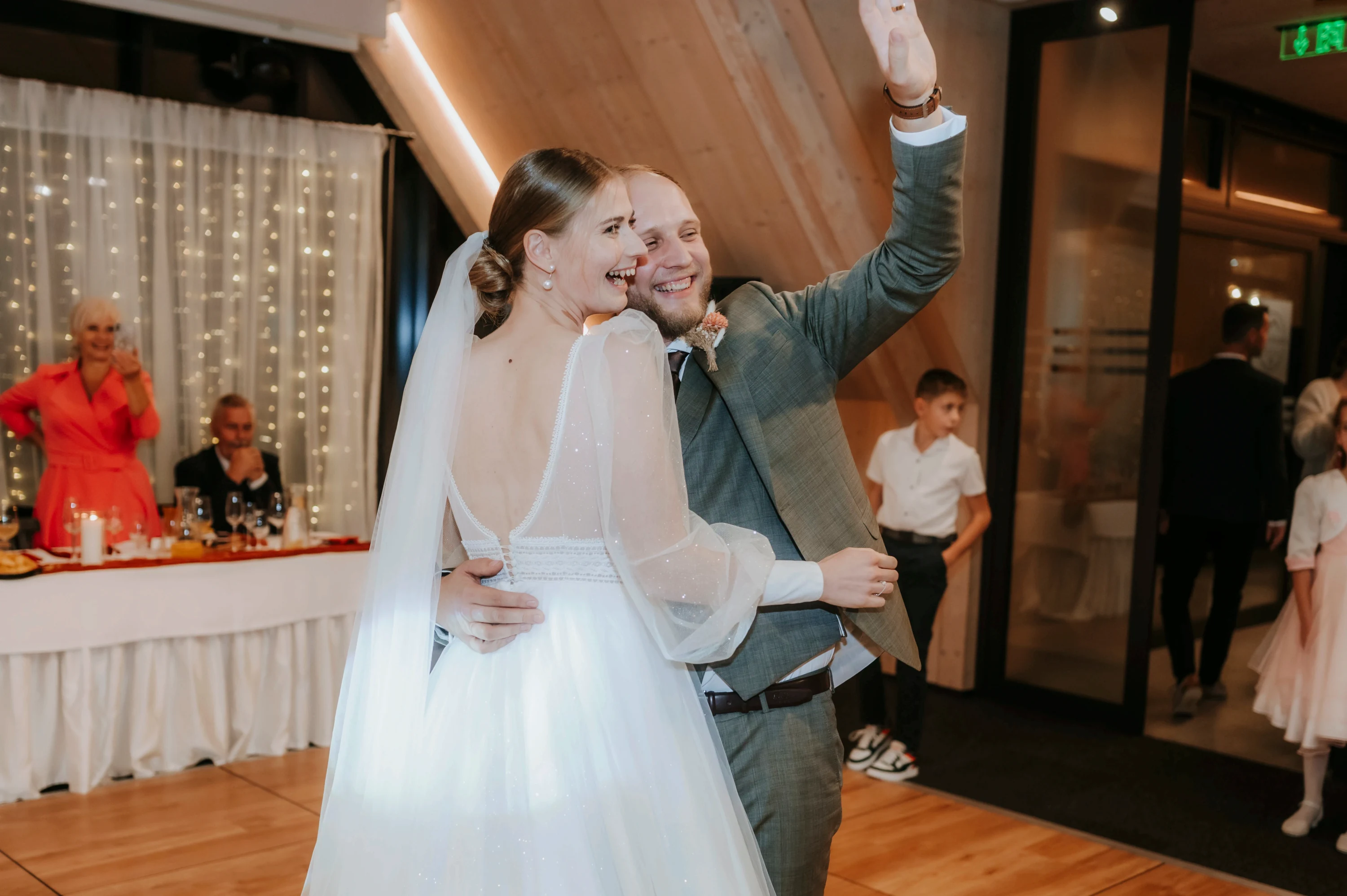 Pár sa raduje so zdvihnutými rukami na svadbe medzi svetlami.