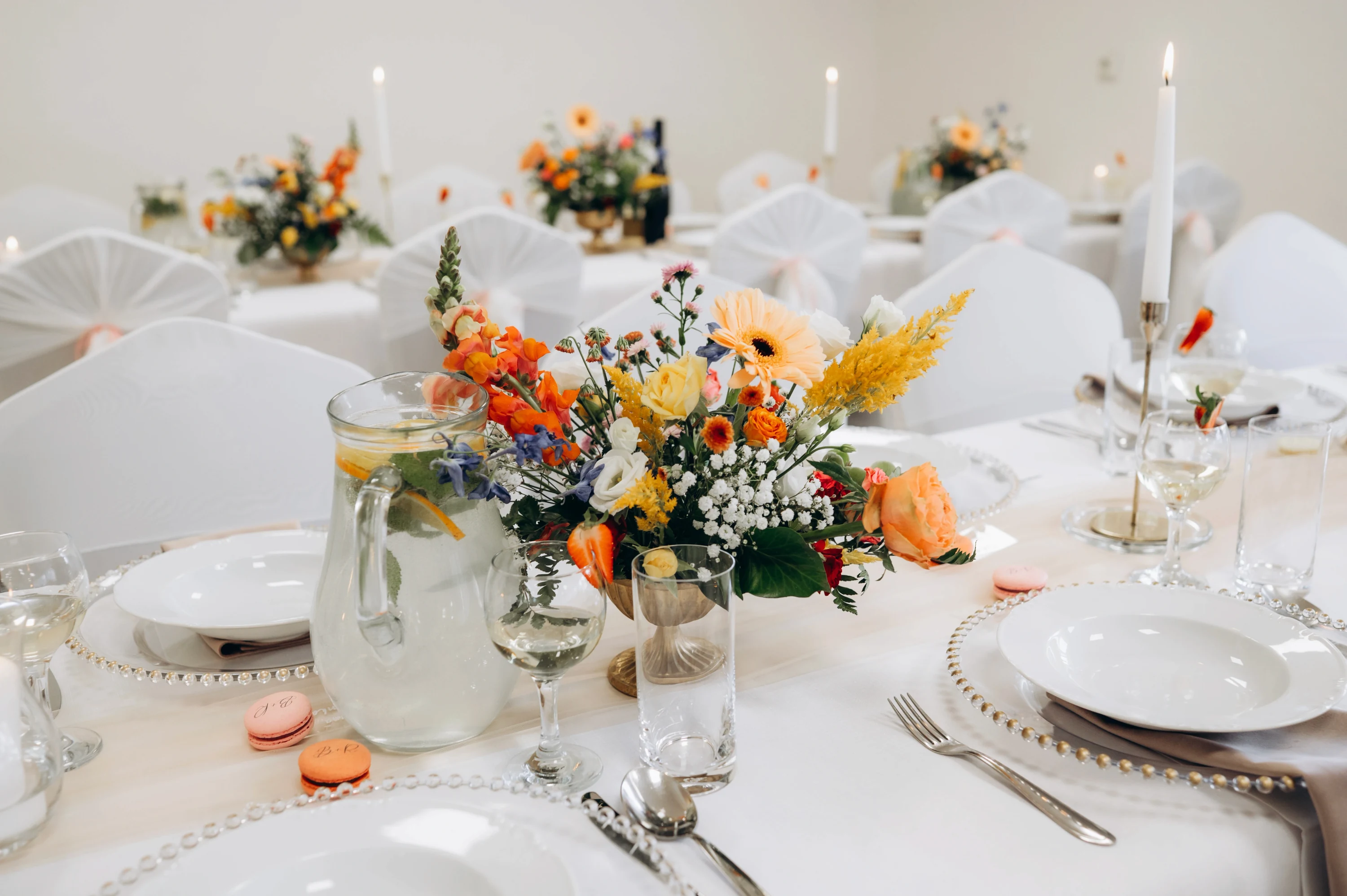 Svadobný stôl zdobený oranžovými kvetinami, sviečkami a elegantným riadom.